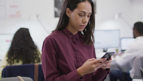 Portrait of smiling biracial businesswoman using smartphone looking at camera in modern office