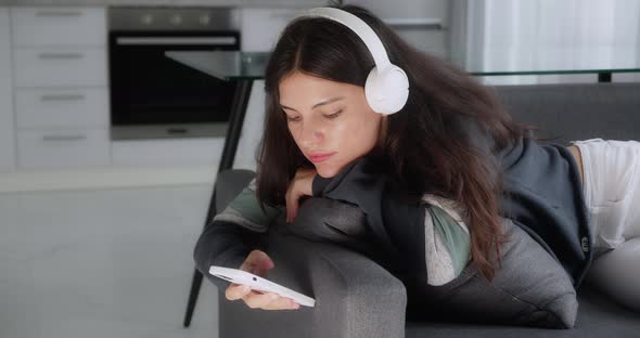 Teenage Brunette Girl Listening to Music Wearing Headphones Relaxing on Sofa Texting Using