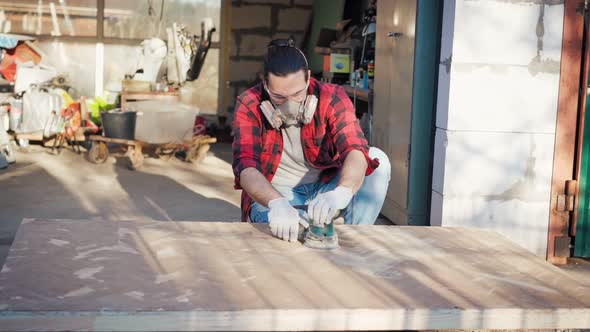 A Young Man in a Construction Respirator Grinds a Parquet Board with a Sander