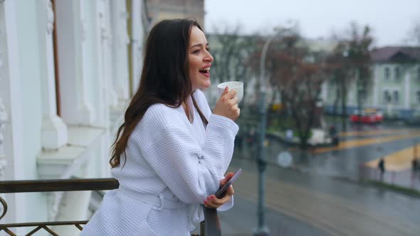 Beautiful young girl in a snow-white terry bathrobe on a balcony with the cup of tea in the morning.