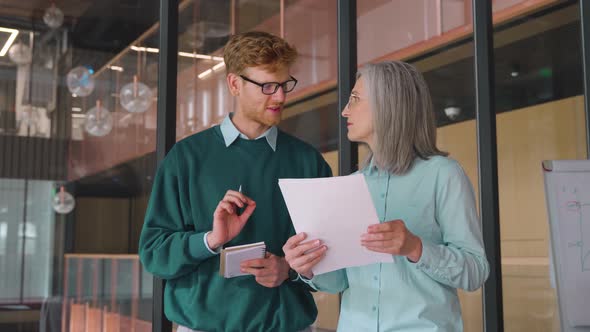 Mature Businesswoman Teaching on Documents Young Male Intern in Office