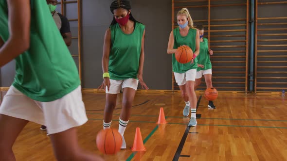 Diverse female basketball team and coach wearing face masks practice dribbling ball