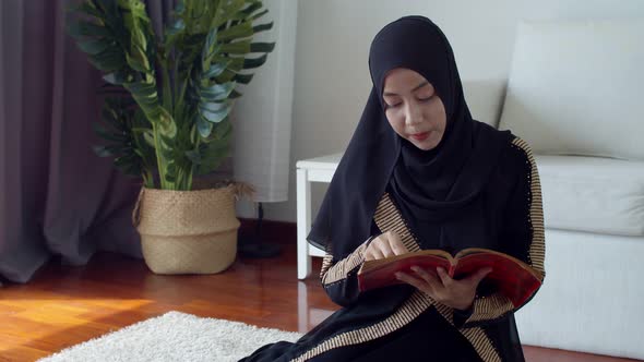 Young Muslim female wearing Islamic clothes reading the Quran