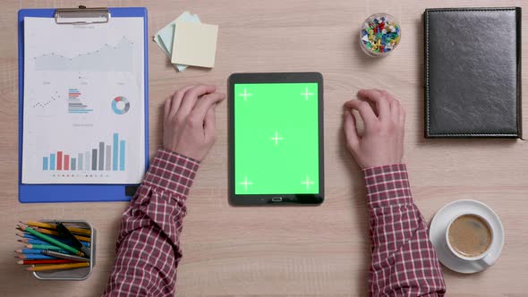 Top View of Male Hands Scrolling on the Top Edge of a Green Screen on a Black Tablet