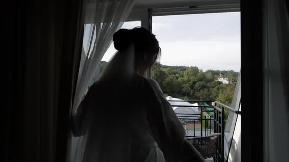 Lovely Bride in White Boudoir Dress Goes To Balcony and Opens Curtains in Hotel Room or Apartment