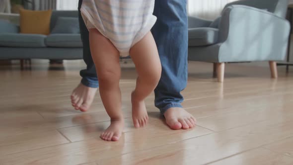 Close Up Father Holding And Helping His Little Baby Learning To Walk On Floor At Home