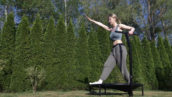 girl does Jumping fitness on trampoline in outdoor on green grass and trees on background