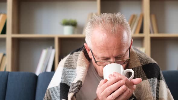 The Old Sick Grandfather Drinks Tea Wrapped in a Blanket Looking Away
