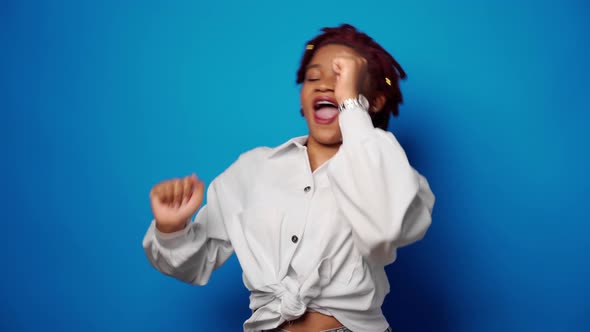 Happy Young Afro American Woman Dancing in Studio Against Blue Background