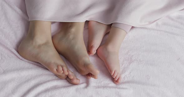 Two Pairs of Legs of the Family in Bed Under the Coverlet - Mother and Baby