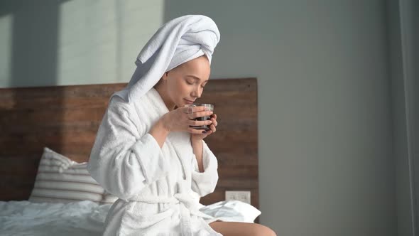 Pretty Woman in a White Coat and Towel Drinking Tea