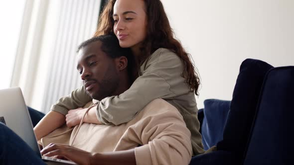 Relaxed Young Couple At Home Sitting On Sofa Browsing Internet On Laptop Computer