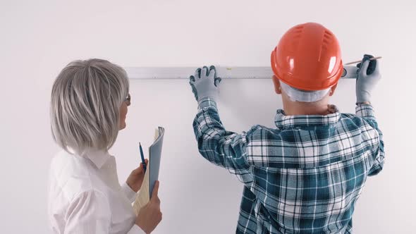 An Elderly Worker in a Helmet and a Female Engineer with a Tablet and a Level in Their Hands Discuss