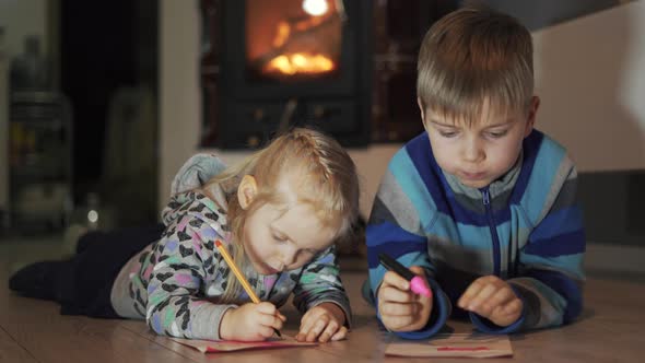 Brother and Sister Lying on the Floor in the Room Writing and Drawing Fireplace in the Background alt