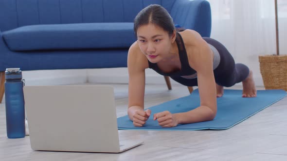 Attractive Asian woman looking laptop practice yoga plank online course at home