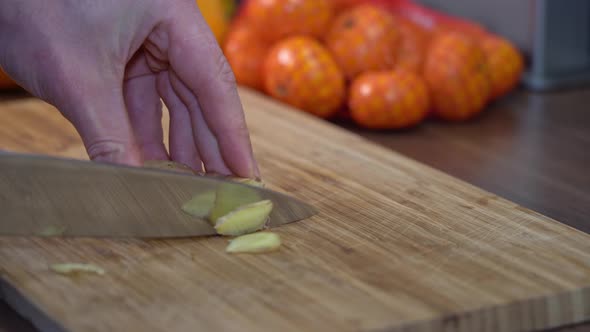 closeup cutting slices of ginger root on wooden chopboard
