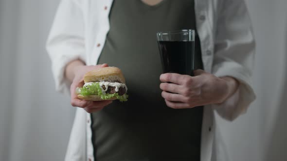 Pregnant Woman with Unhealthy Sandwich and Soda Water Standing Indoors