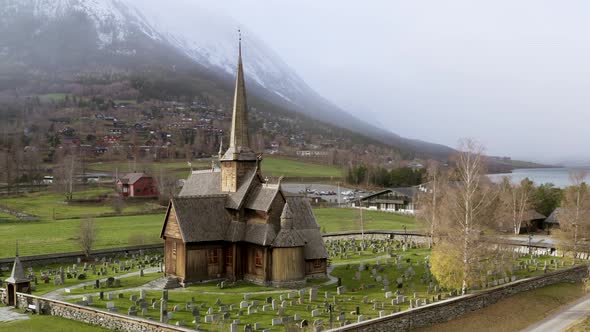 Lom Stave Church With Snowy Mountain In The Background During Autumn Blizzard In Norway. - aerial