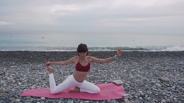 Female Gymnast Is Stretching Hands and Legs on Pebble Sea Beach in Daytime