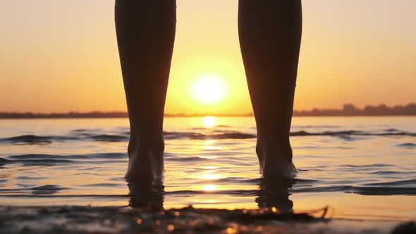 Silhouette of Woman Legs Standing in Water at Sunset on Beach. Slow Motion