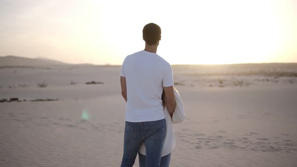 Young Couple Standing and Hugging Man Holding Her Woman From the Back on the Dried Sandy Desert