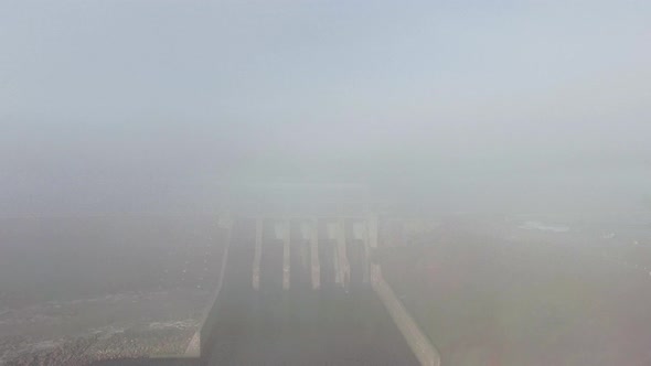 Drone moves into the fog from a white dam (Mactaqac dam, New Brunswick, Canada)