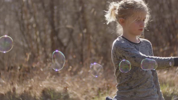 Boy Using Bubble Wand To Make Bubbles In Sunlit Field