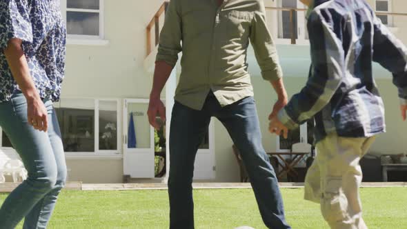 Happy senior caucasian couple with grandson playing football in garden