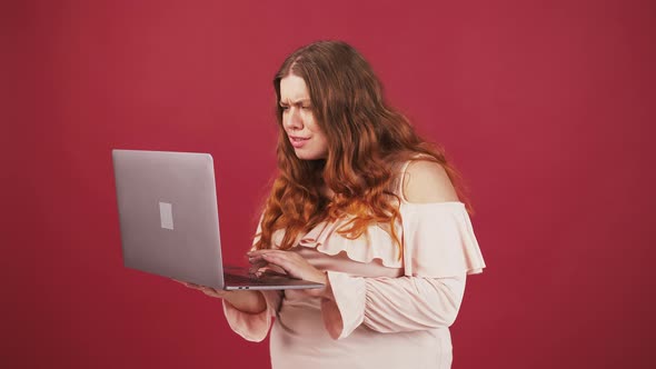 Excited Plus Size Woman Looking at Laptop Screen Raising Hand with Excitement Red Studio Background