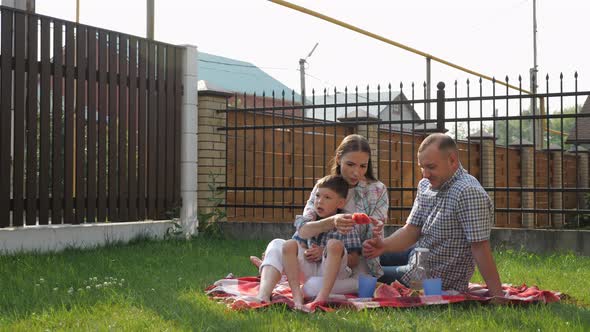 Happy Young Woman and Man Sit with Little Boy on Lawn