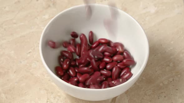 Red beans falling in a white bowl 
