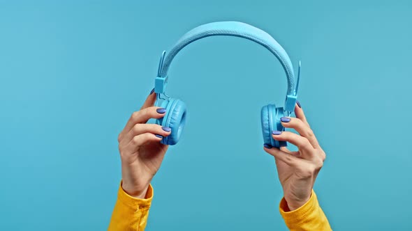 Hands of Woman with Wireless Headphones Isolated on Blue Studio Background