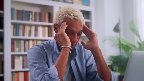 Young African American Man Doing Massage Temples Sits with Laptop in Library