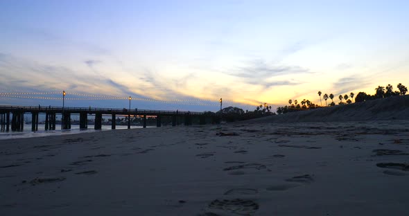 Stearns Wharf pier at sunset with people walking on the boardwalk viewed from the sandy beach below