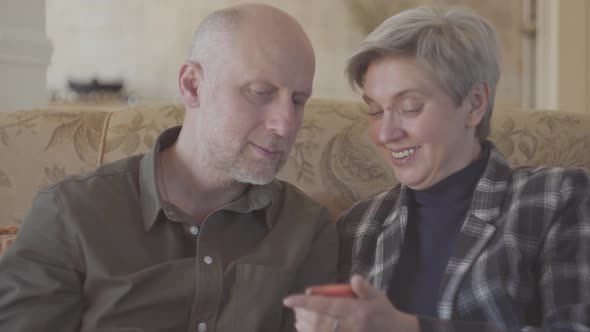 Adult Couple Sitting on the Big Sofa and Bald Woman Showing Photos in the Mobile Phone<