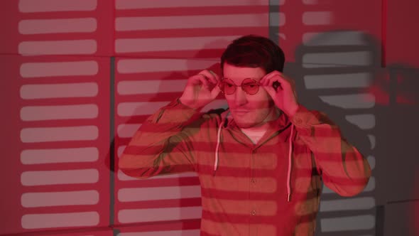 Man Puts on Glasses Standing Near Wall with Shadows of Jalousie