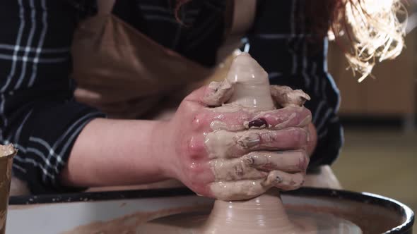 A Woman Artist Forms Clay in a Longer Shape on a Potter's Wheel