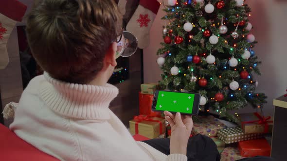 A man enjoying wine and scrolling Green Screen Mockup phone in a Chrismas decorated living room.