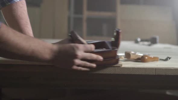 Hands of a Carpenter in a Workshop with a Plane Flies Shavings