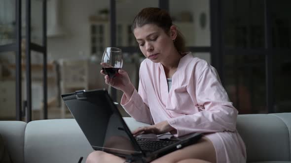 Young woman resting after work at home with glass of wine and laptop