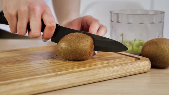 Female Hands Cut the Kiwi with a Knife on 2 Half on a Wooden Board