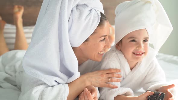 Portrait of a Mother and Little Daughter on the Bed with a Remote Control in Their Hands, Switching