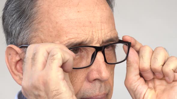 An Elderly Man Squints Puts on His Glasses