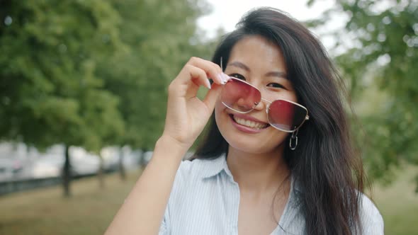 Portrait of Asian Girl Taking Off Sunglasses in Park Smiling Looking at Camera