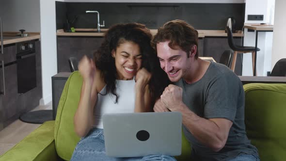 Excited Overjoyed Multiracial Couple Look at Screen of Laptop Feel Winners Surprised By Lottery