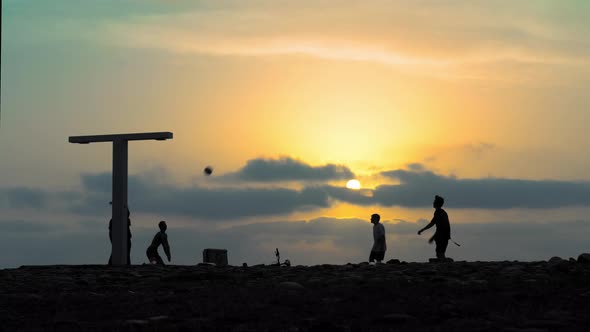 Silhouette of active young people playing volleyball against backdrop of sky by sea