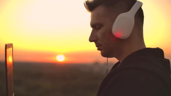 A Man in Headphones on the Roof Relaxes Working Remotely Enjoying Life Despite a Handsome Kind of