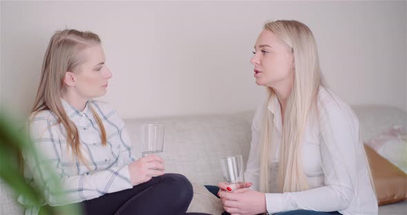 Two Women Drinking Water in Living Room Talking and Smiling.