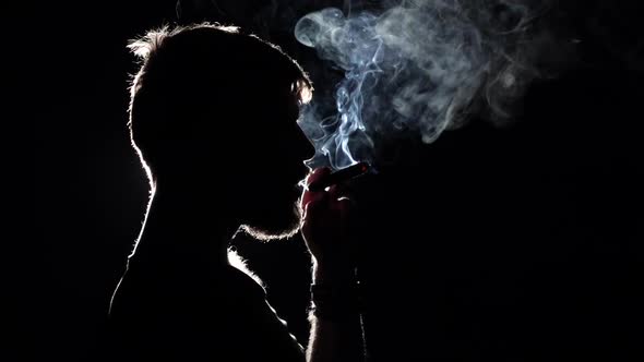 Brutal Man Smokes a Cigar. Takes a Big Drag and Puffs Smoke. Blacklight. Silhouette. Close Up. Slow