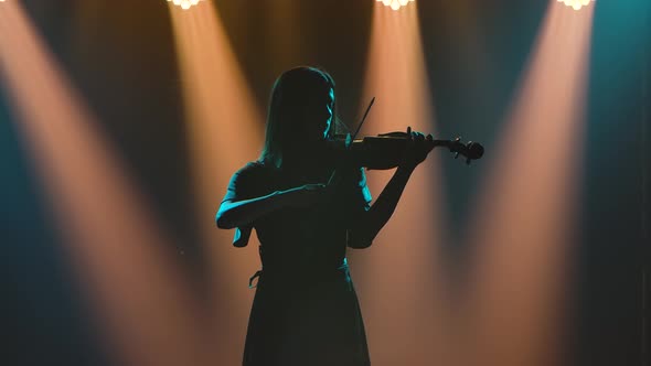 A Dark Silhouette of a Woman Playing the Violin. Magical Studio Light in the Background. Slow Motion
